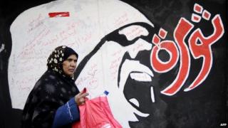 A woman walks past graffiti which reads 'revolution'
