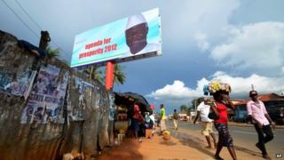 People walk past a campaign poster for incumbent President Ernest Bai Koroma, in Freetown, Sierra Leone, Friday, Oct. 19, 2012.
