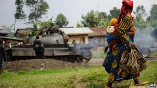 A displaced woman carrying her child walks past an army tank in eastern Democratic Republic of Congo (26 July 2012)
