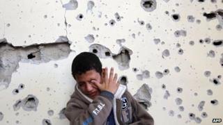 Palestinian boy cries as he sits outside his home which was damaged following an Israeli air strike