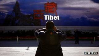 A man taking a photograph in front of a screen displaying propaganda about China's Tibet Autonomous Region in Beijing, 12 November 2012