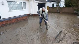 Tom Wynne sweeps muddy sediment off the drive of a home after flood waters receded in St Asaph