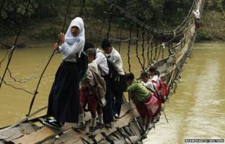 Students hold on to the side steel bars of a collapsed bridge as they cross a river to get to school at Sanghiang Tanjung village, Indonesia, 19 January 2012