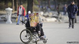 An elderly woman in a wheelchair reads on her own in a park in Beijing