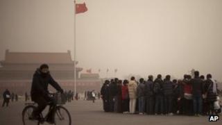 A police officer in plain clothes rides a bicycle past tourists pose for a group photo on Tiananmen Square on a hazy day in Beijing, China, 28 February 2013