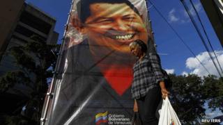 A woman walking past a poster of Hugo Chavez