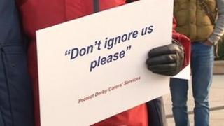A Derby carer holding a sign which reads "Don't ignore us please"