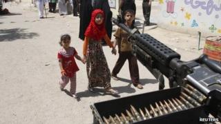 Children walk past a machine-gun in Baghdad (20 April 2013)