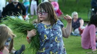 A girl dances while wearing face paint and holding a sheaf of grass