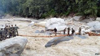 Indian defence personnel assist stranded civilians in crossing a raging river near the Pindari Glacier area of northern Uttarakhand state on 27 June 2013