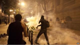 A demonstrator throws a tear gas canister back at police during a protest in Rio, 11 July