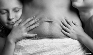 A photo taken by Jade Beall of a mother with her two children cuddling her stomach as part of her A Beautiful Body project