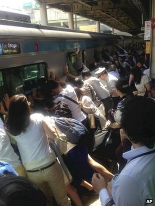 Train passengers and railway staff push a train car to rescue a woman stuck between the car and the platform at Japan Railway Minami Urawa Station in Saitama, near Tokyo, on 22 July 2013