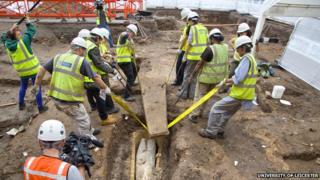 Eight people lifting the lid of the stone coffin