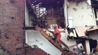 A firefighter and dog search the partially collapsed property