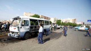 Air force troopers walk by a bus hit by the bomb attack in Sanaa