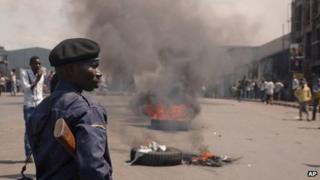 A police officer looks on as protestors burn tires in the street following recent violence, including mortar attacks that have struck homes and churches in the eastern provincial capital, killing at least seven civilians and wounding dozens of others, in Goma, Congo, Saturday, Aug. 24, 2013.