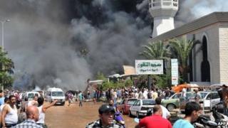 Smoke is seen above people gathering outside a mosque on the site of a powerful explosion in the northern Lebanese city of Tripoli on 23 August, 2013.