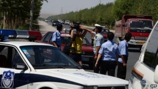 Chinese police detain a journalist at a checkpoint on the road to the riot-affected Uighur town of Lukqun, Xinjiang province, on 28 June 2013