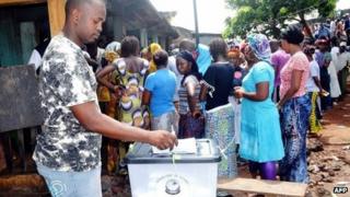 A Guinean voter casts his ballot as others queue at a polling station in Conakry on 28 September 2013
