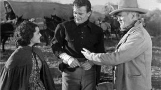 John Wayne standing between two people in The Oregon Trail