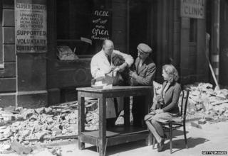A vet treats a dog outside after his premises are blown out by a bomb. A sign reads: "Animals humanely destroyed"