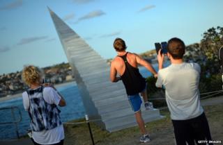 A man poses before a sculpture of stairs that lead into the sky