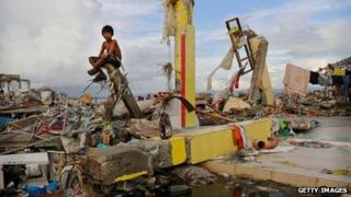 A young boy sits on the ruins of a building amid scenes of devastation in the aftermath of Typhoon Haiyan in Tacloban, Leyte, Philippines
