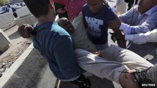 People carry a man who injured when Libyan militiamen opened fire into a crowd of protesters in Tripoli 15 November, 2013