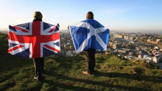 Two people holding up a Scottish and a Union flag