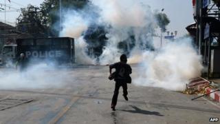 An anti-government protester runs as police fire tear gas shells at them outside the Government house during a demonstration in Bangkok on 2 December 2013