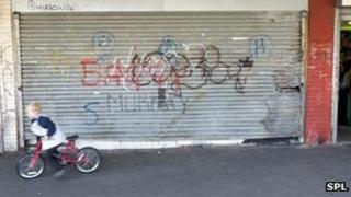 Boy on bicycle rides past graffiti on a shop front
