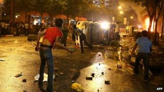 Young men hurt large stones from behind an overturned police van in Little India, Singapore