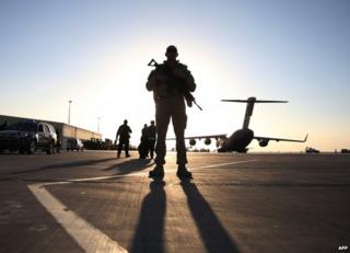 A US soldier stands guard near a plane on a runway at Kandahar air base, 8 December