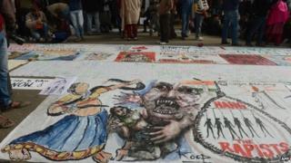 In this photograph taken on December 30, 2012, Indian bystanders look at a banner featuring images of "government and rapists" as it lies on a road in New Delhi