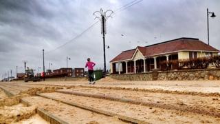 Jogger on sand covered Felixstowe promenade