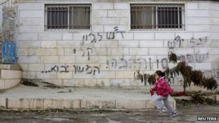 A girl runs past graffiti on a house in the West Bank village of Dahiyat al-Zira that reads: "Regards to John Kerry - to be continued" (31 December 2013)
