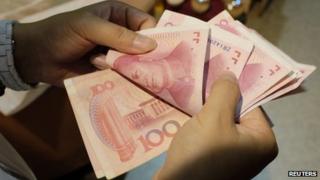 File photo: A woman counts Chinese yuan notes at a market in Beijing, 1 July 2013
