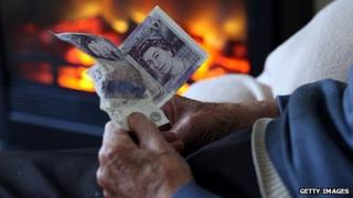 An elderly man holding cash in front of a gas fire