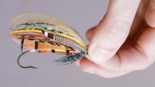 Fingers holding a fishing fly