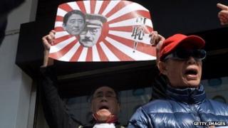 A protester in Hong Kong holds up a sign with photos of current Japanese Prime Minister Shinzo Abe and World War II Prime Minister Hideki Tojo.