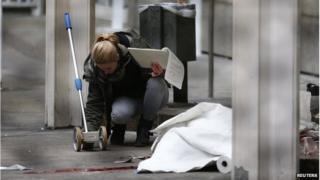 A police officer examines the crime scene next to a covered body, after a double murder at the state court in Frankfurt.