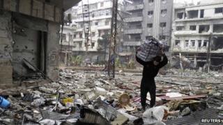 A man carries a bag amid damage and debris in the besieged area of Homs
