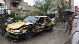People walk past the scene of a car bombing in Hurriya, Baghdad (3 February 2014)