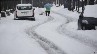 A woman walks with dog on the snow-covered road in Yokohama, near Tokyo Saturday, Feb. 15