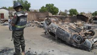 A Nigerian policeman stands guard by burned out cars and houses, following an attack by suspected Islamic extremists in Kawuri, Maiduguri, Nigeria, Tuesday, Jan. 28, 2014.