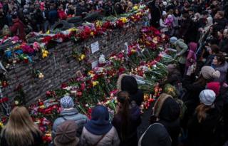 People standing at a memorial covered in flowers in Independence Square