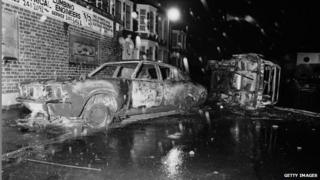 Cars left overturned and burned-out in the street after rioting on the Broadwater Farm housing estate