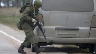 An unidentified gunman searches a vehicle while he and others block the road toward the military airport at the Black Sea port of Sevastopol