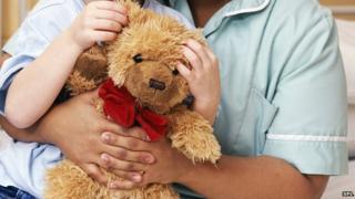 A teddy bear being cuddle by child and nurse